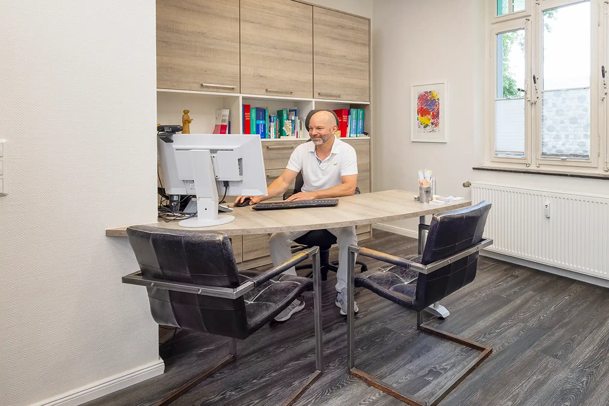 Arzt sitzt am Schreibtisch in seinem Büro – Ansprechpartner für häufige Fragen (FAQ) der Praxis Poststraße 7 Mudersbach